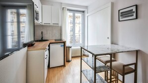 A compact kitchen with a small refrigerator, a sink, and a window overlooking a building. - 33.Studio 2Pers#Sèvres-Lecourbe#Champ-de-Mars (Paris)