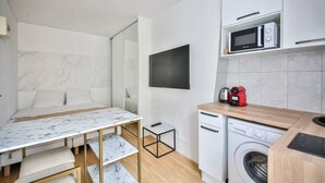A compact bedroom with a bed, a small bedside table, a TV, and a washing machine. - 33.Studio 2Pers#Sèvres-Lecourbe#Champ-de-Mars (Paris)