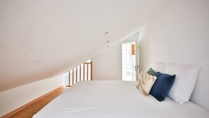 A bedroom with a sloped ceiling, a bed with pillows, and a wooden floor. - 01.Duplex near Tour Eiffel & Montparnasse Station (Paris)