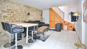 A modern living space with a stone wall, a wooden staircase, a dining area with a table and chairs, and a black leather sofa. - 01.Duplex near Tour Eiffel & Montparnasse Station (Paris)