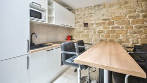 A compact kitchen with white cabinets, a microwave, a wooden table, and black chairs. - 01.Duplex near Tour Eiffel & Montparnasse Station (Paris)
