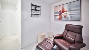 A modern room with a leather chair, a white door, a black shelf, and a large abstract painting on the wall. - 02.Duplex#2Bedrooms#Sèvres-Lecourbe#Champ-de-Mars (Paris)