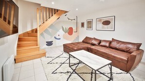 A living room with a brown leather sofa, a white coffee table, and a wooden staircase. - 02.Duplex#2Bedrooms#Sèvres-Lecourbe#Champ-de-Mars (Paris)