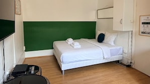 Hotellihuone, jossa on sänky, vihreä korosteseinä, valkoinen kattovalaisin ja valkoinen kaappi.