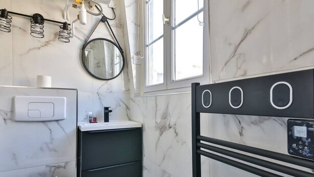 Un baño moderno con pared de mármol, tocador negro, espejo, inodoro y toallero negro con pantalla digital.