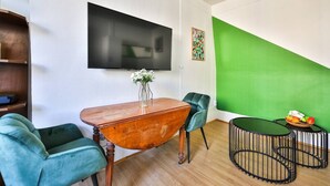 A modern living room with a wooden dining table, two green chairs, a black TV mounted on the wall, and a green accent wall. - 41.Studio 2Pers#Sèvres-Lecourbe#Necker (Paris)