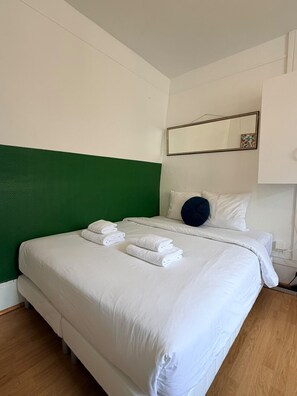 A hotel room with a large bed, a green accent wall, a mirror, and neatly folded towels.