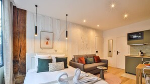 Moderni hotellihuone, jossa on suuri sänky, sohva, pieni pöytä ja pieni keittiönurkkaus.