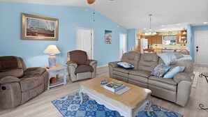 A living room with a ceiling fan, a sofa, a coffee table, and a dining area with a kitchen in the background. - Ranch Retreat: Luxury Living in Village Charm! (The Villages)