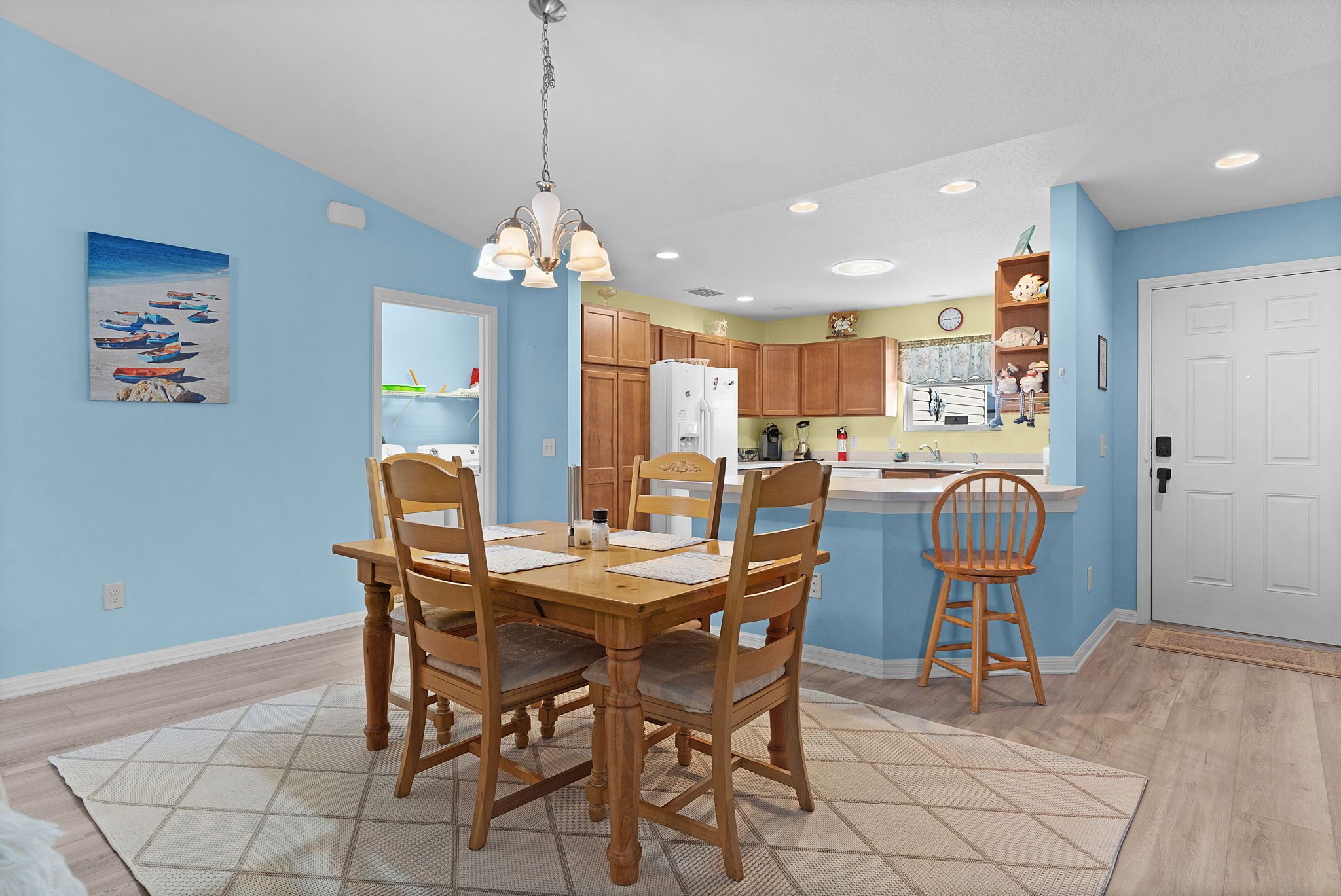 A dining area with a wooden table and chairs, a kitchen with wooden cabinets, and a blue wall.