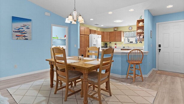 A dining area with a wooden table and chairs, a kitchen with wooden cabinets, and a blue wall. - Ranch Retreat: Luxury Living in Village Charm! (The Villages)
