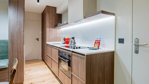 Een kleine keuken met houten kastjes, een inbouwoven en een aanrecht met een waterkoker en een cornflakes doos.