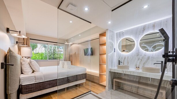 Een moderne slaapkamer met een bed, een douchecabine van glas en een wastafel met spiegel.