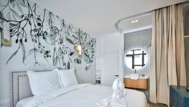 Een net opgemaakt bed in een hotelkamer met een groot raam, een wandlamp en uitzicht op de badkamer.