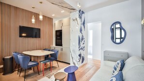 Een moderne woonkamer met een ronde eettafel, blauwe stoelen, een grijze bank en een bijzonder kunstwerk aan de muur.