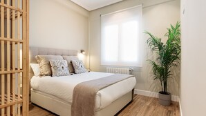 A bedroom with a bed, a wooden crib, a potted plant, and a window with blinds. - Genteel Home Jovellanos Terrace (Gijon)