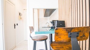 A small kitchenette with a coffee maker, toaster, and sink. There are two stools and a chair with a wooden backrest. - Typical Parisian Studio in Le Marais (Paris)