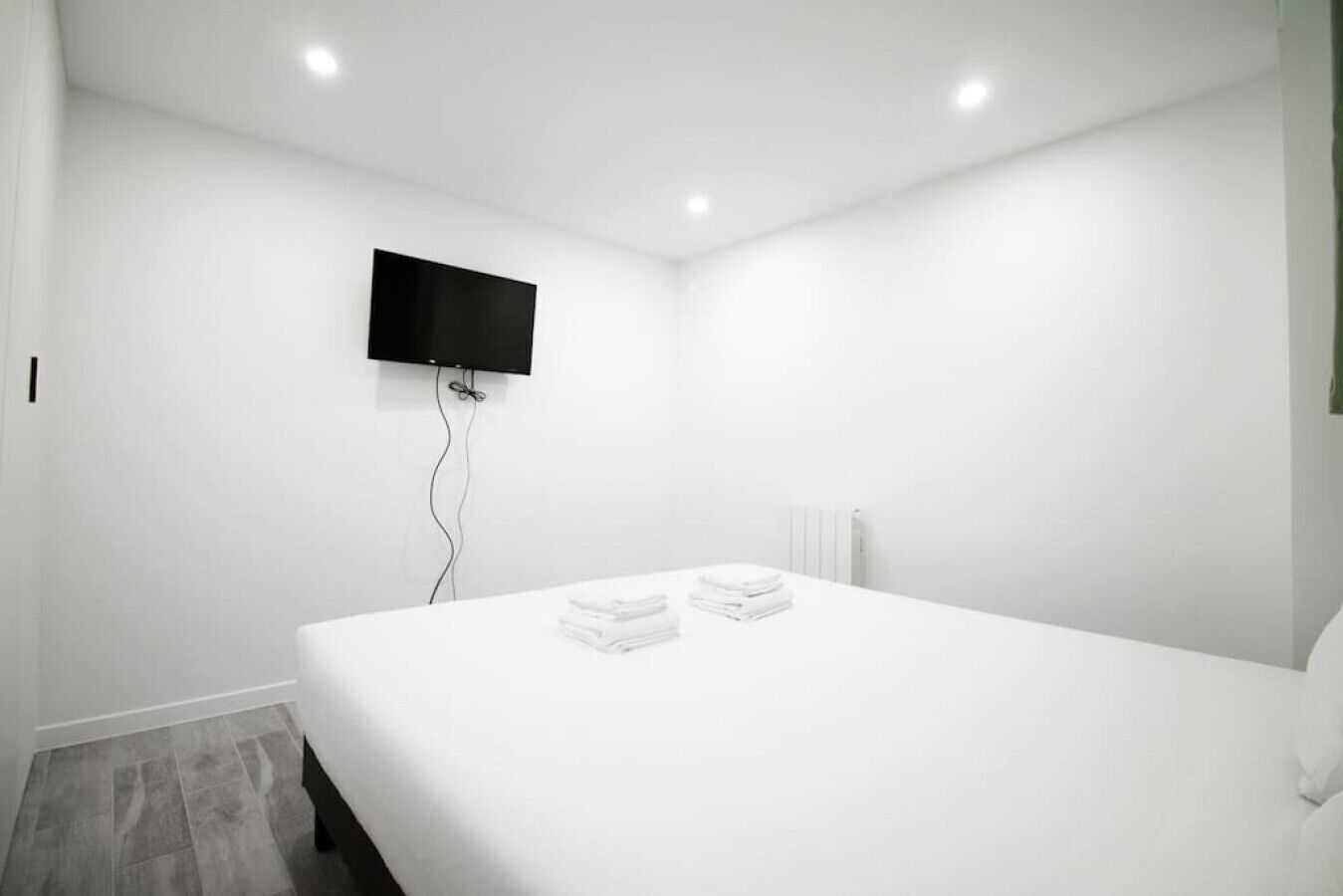 Een minimalistisch hotelkamer met een groot bed, een flatscreen televisie aan de muur en een radiator.