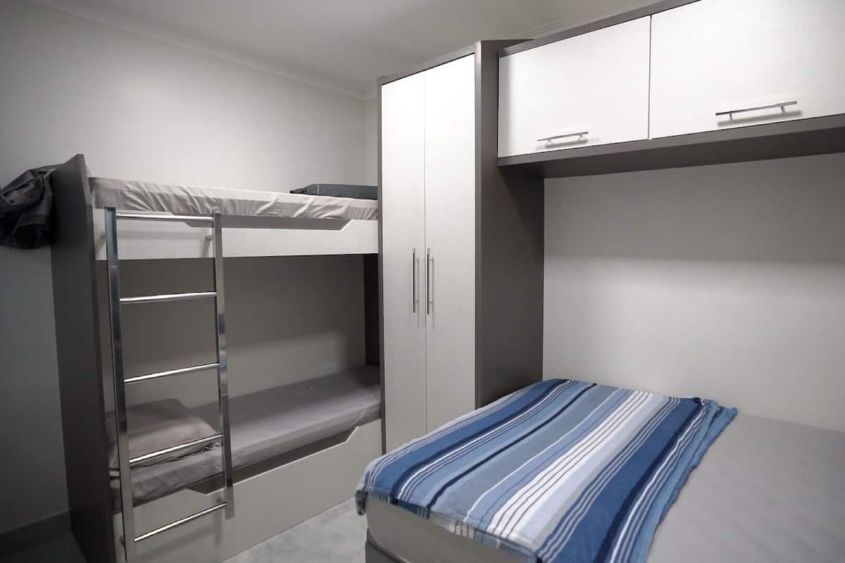 Una cama litera con escalera, una cama individual con una colcha a rayas y un armario de dos puertas.