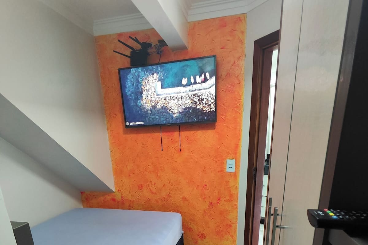 Una habitación con una cama, un televisor montado en la pared y una puerta que da a otra estancia.