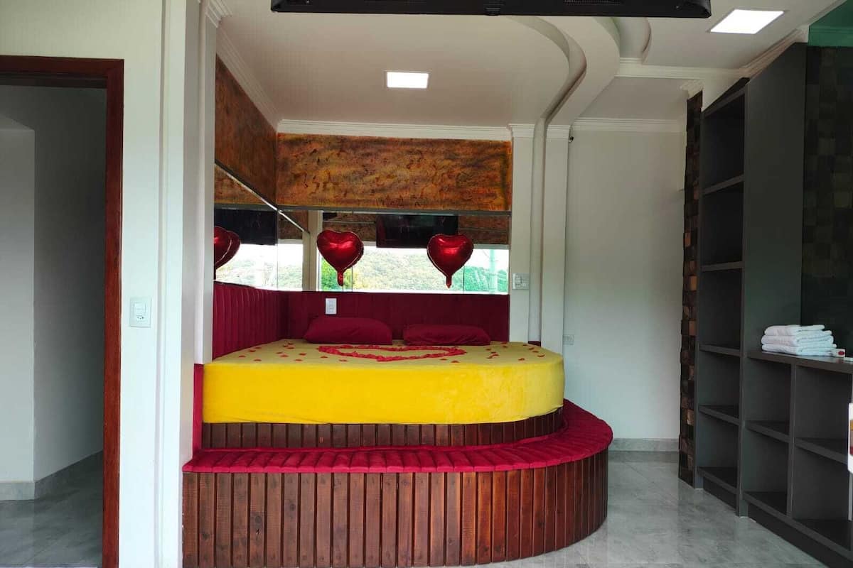 Una cama redonda con colchón amarillo y ropa de cama roja, cabecera de madera y adornos con forma de corazón.