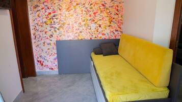 Una habitación con una cama, un muro abstracto y colorido, y un suelo de baldosas.
