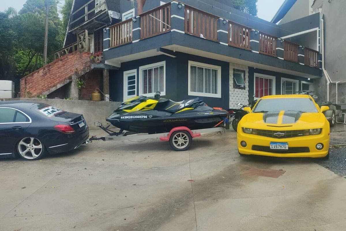 Zona residencial con una casa, un coche deportivo amarillo y un coche negro estacionados frente a ella.