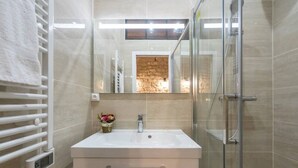 Een moderne badkamer met een douchecabine van glas, een witte wastafel met een wasbak en een handdoekrek.