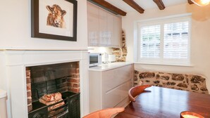 A cozy kitchen with a fireplace, white cabinets, a stone accent wall, and a dining table with chairs. - 36 Main Street (Derby)