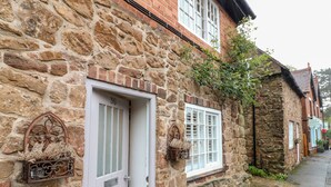 A stone building with a white door, a window with a white frame, and a small hanging planter with dried flowers. - 36 Main Street (Derby)