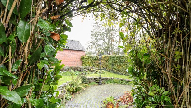 A cobblestone pathway leading to a brick building surrounded by lush greenery and a hedge. - 36 Main Street (Derby)