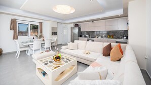 Ein modernes Wohnzimmer mit einem weißen Sofa, einem Couchtisch und einem Essbereich mit weißem Tisch und Stühlen.