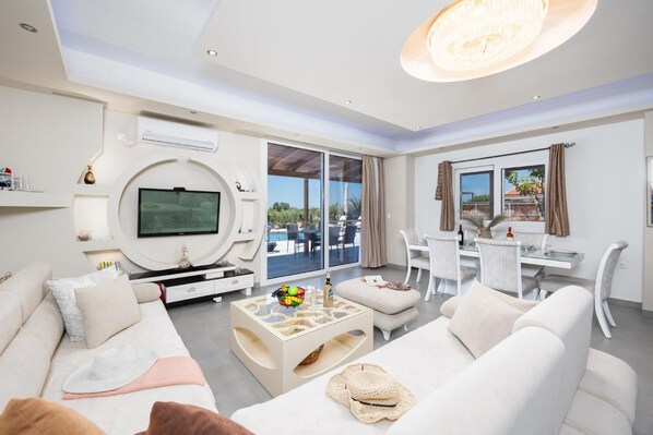 Een moderne woonkamer met een televisie, bank, salontafel en een eethoek.