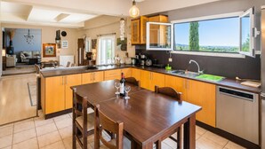 A modern kitchen with wooden cabinets, a dining table, and a large window. - Villa Mavrikia - Four Bedroom Villa, Sleeps 8 (Sfakera)