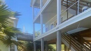Un edificio moderno con un área exterior cubierta, un camino y un pequeño jardín con una palmera.