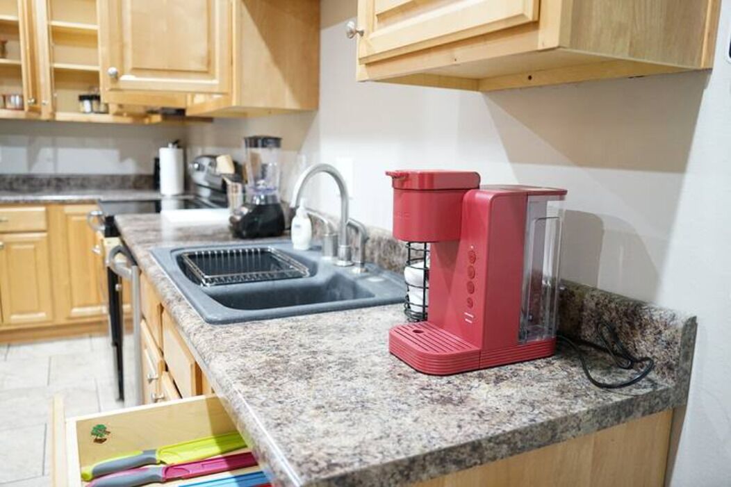 A kitchen with wooden cabinets, a granite countertop, a red coffee maker, and a sink.