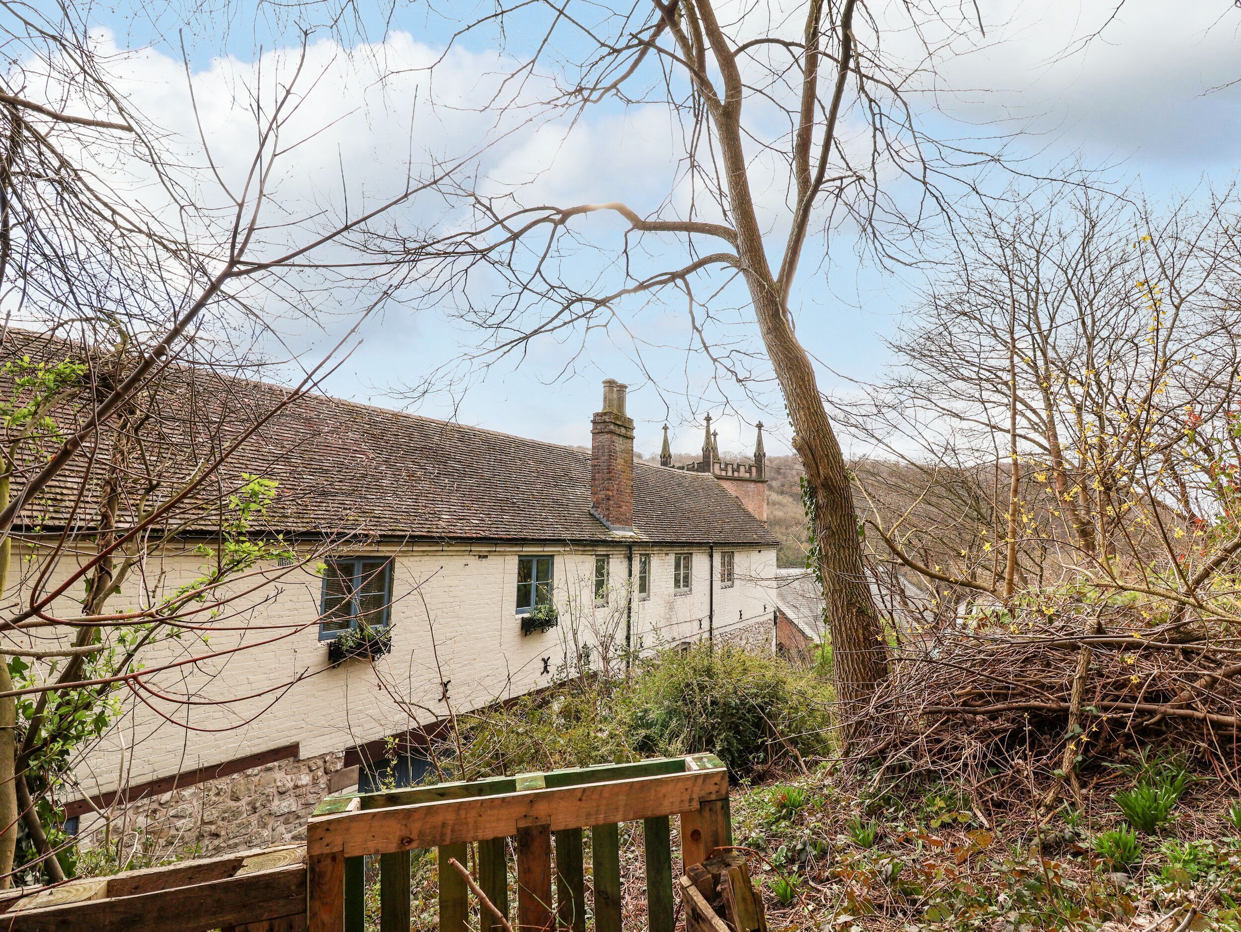 A traditional house with a tiled roof, a stone wall, and a wooden fence.