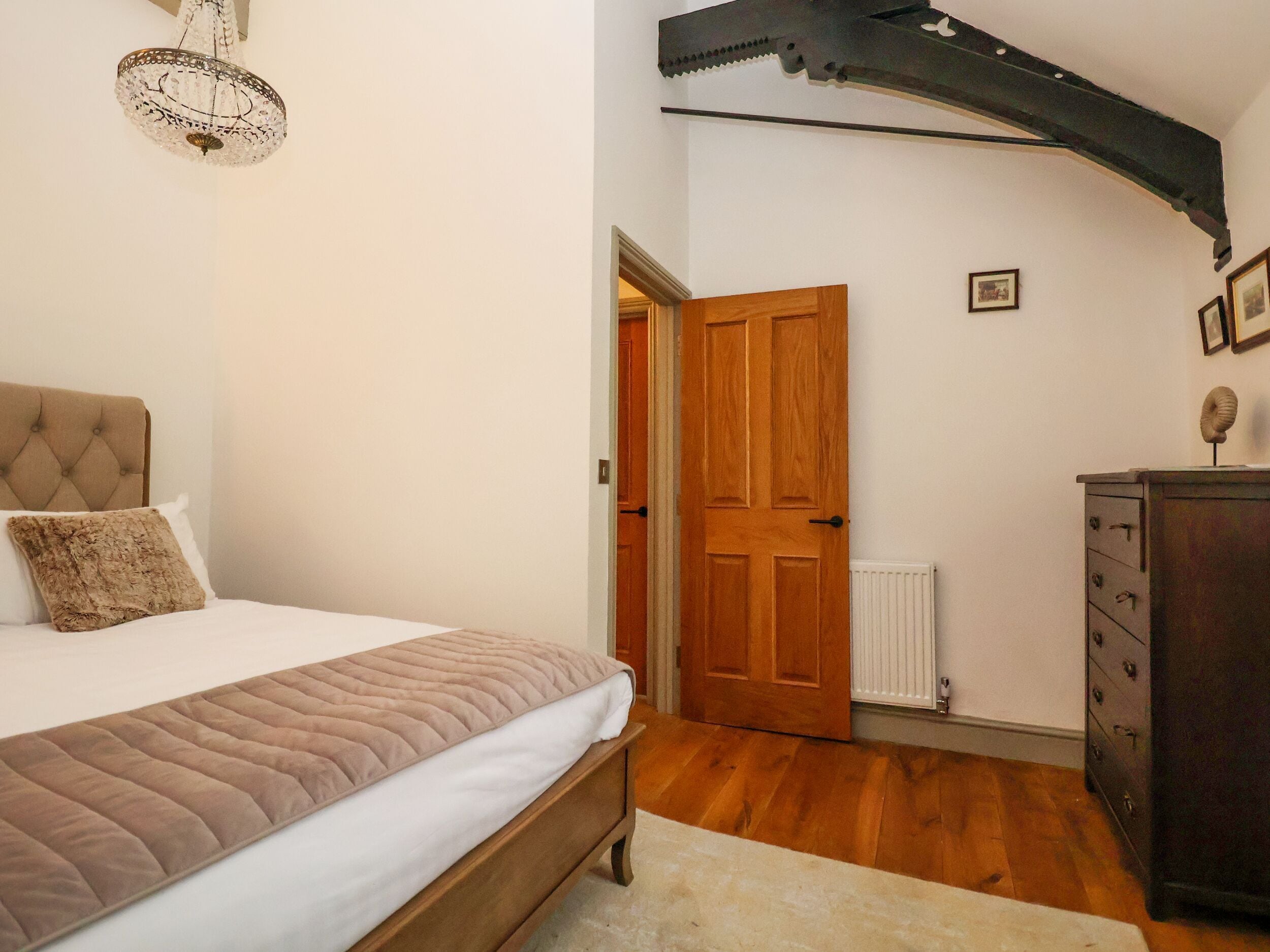 Une chambre à coucher avec un lit, une commode en bois, une porte et un lustre.