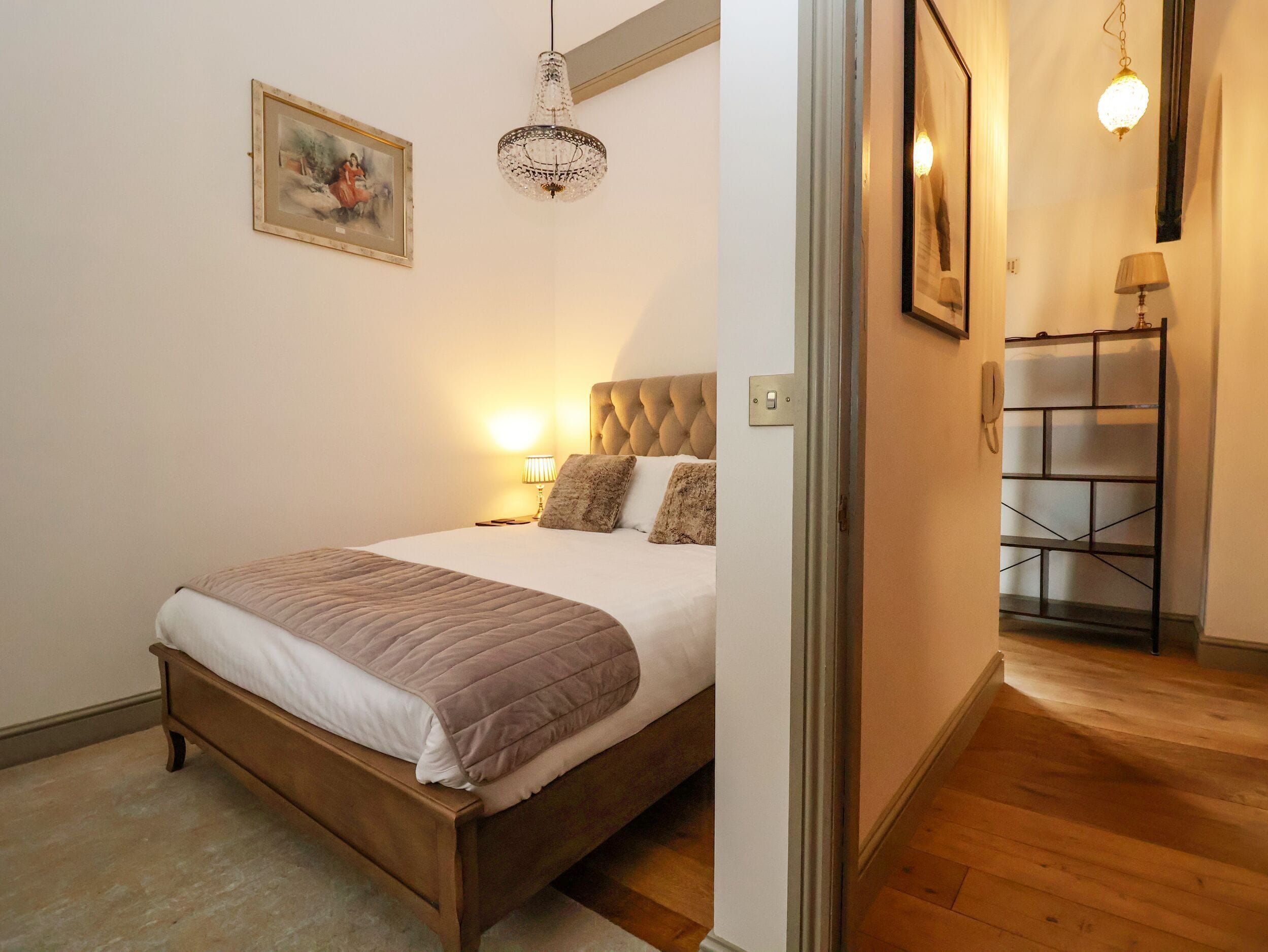 Une chambre à coucher avec un lit, des lampes de chevet, un lustre, un tableau encadré et un plancher en bois.