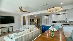 A modern living room with a wooden dining table, striped sofas, and a chandelier.