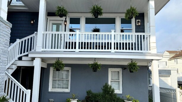 A two-story house with a white porch, a staircase, and potted plants.