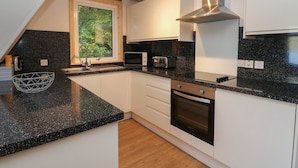 A modern kitchen with a black granite countertop, white cabinetry, a stainless steel range hood, and a window with a view of greenery. - 27 Invergarry Lodges (Invergarry)