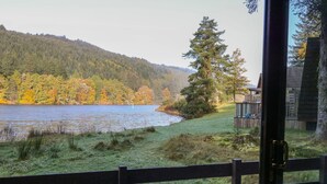 A lakeside view with a wooden fence, a grassy area, and a forested hill in the background. - 27 Invergarry Lodges (Invergarry)
