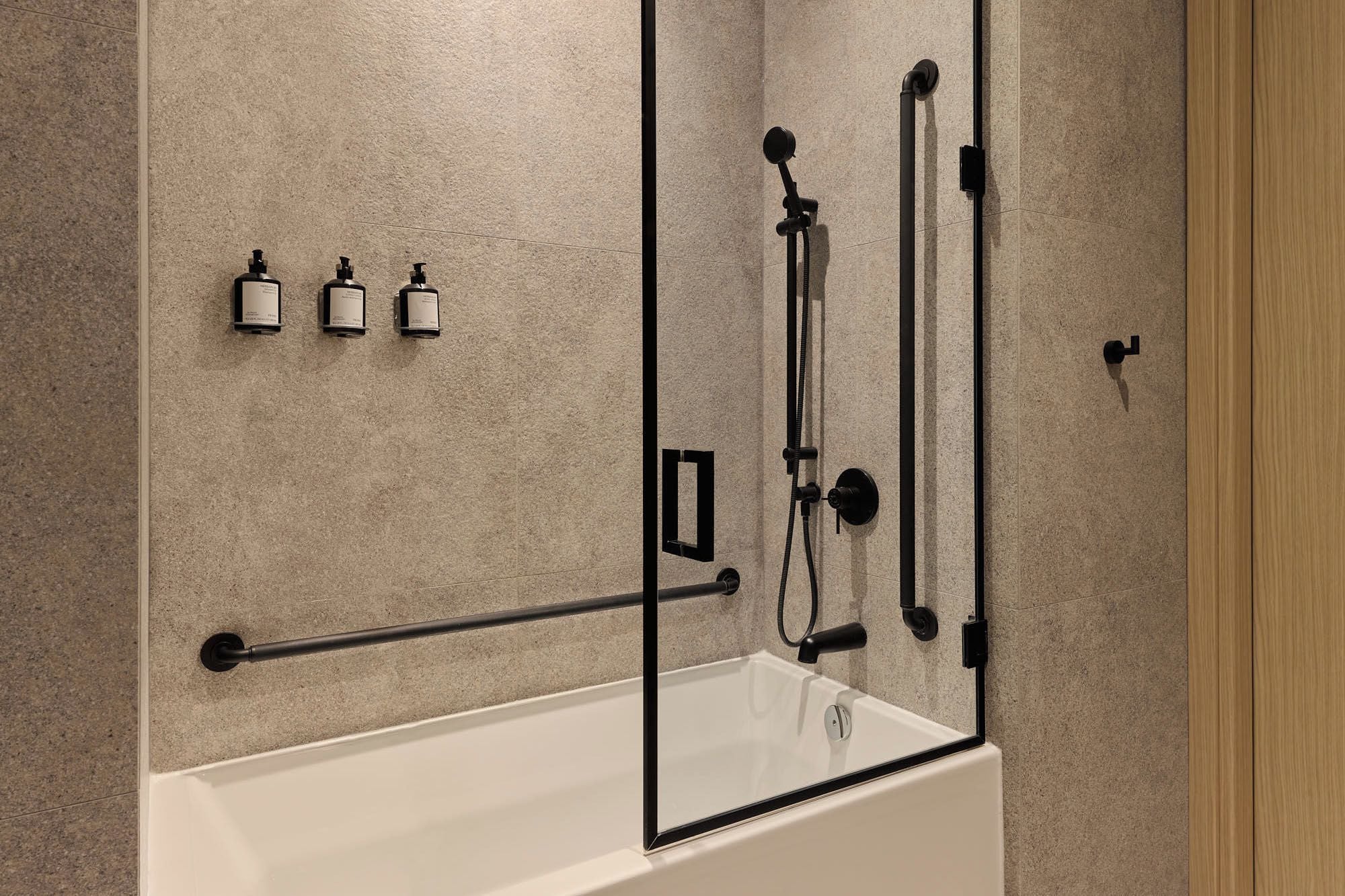Un bagno moderno con una vasca, un sistema doccia e tre flaconi di shampoo.