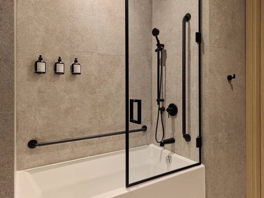 A modern bathroom with a bathtub, a shower system, and three bottles of shampoo.