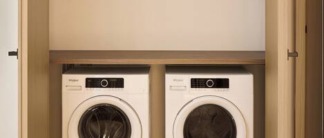 A laundry room with two white Whirlpool washing machines, wooden flooring, and a wooden door.