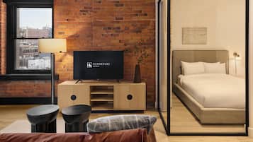 A hotel room with a brick wall, a television, a bed, a window, and a view of buildings outside.