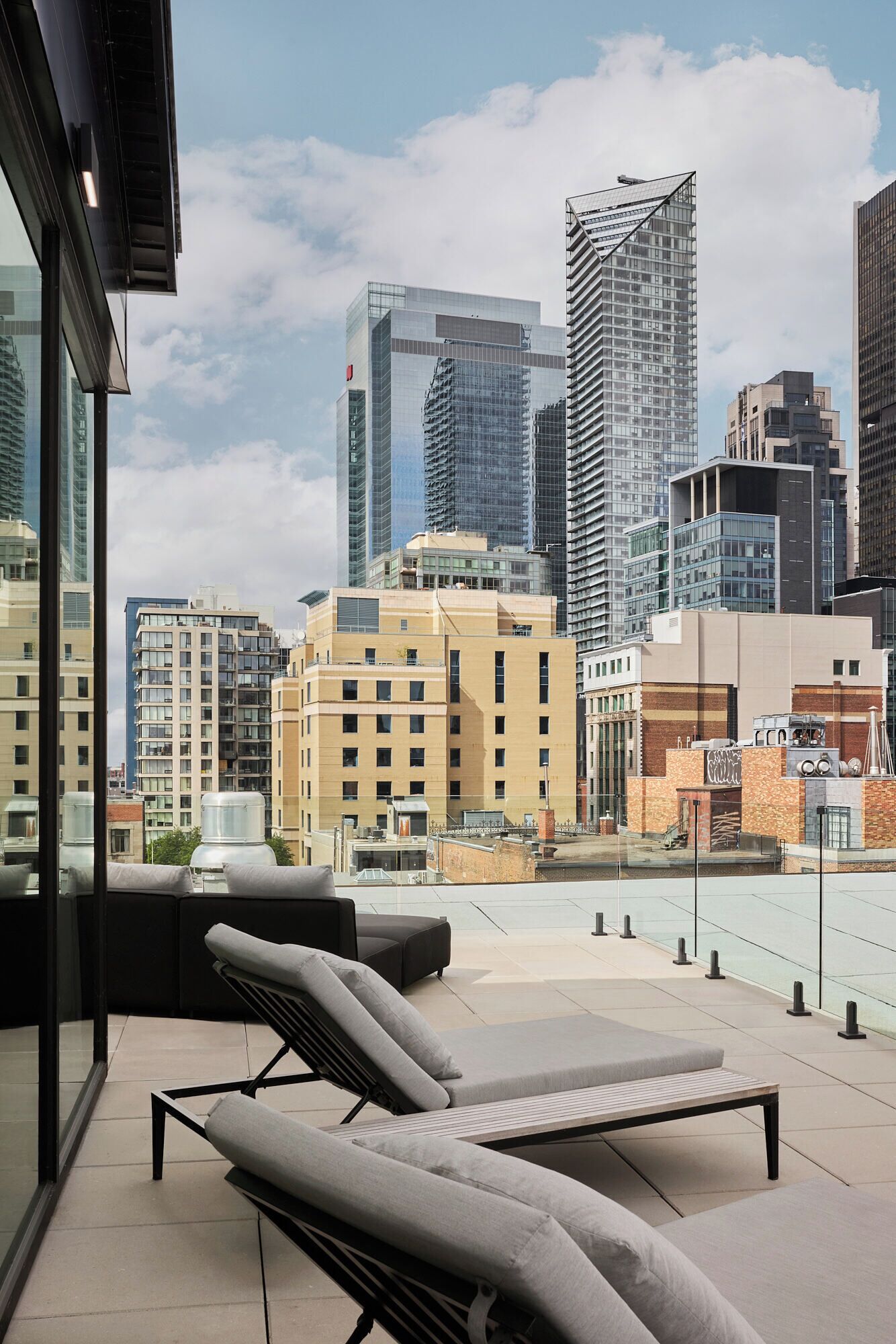 A rooftop terrace with lounge chairs, a glass balustrade, and a city skyline view.