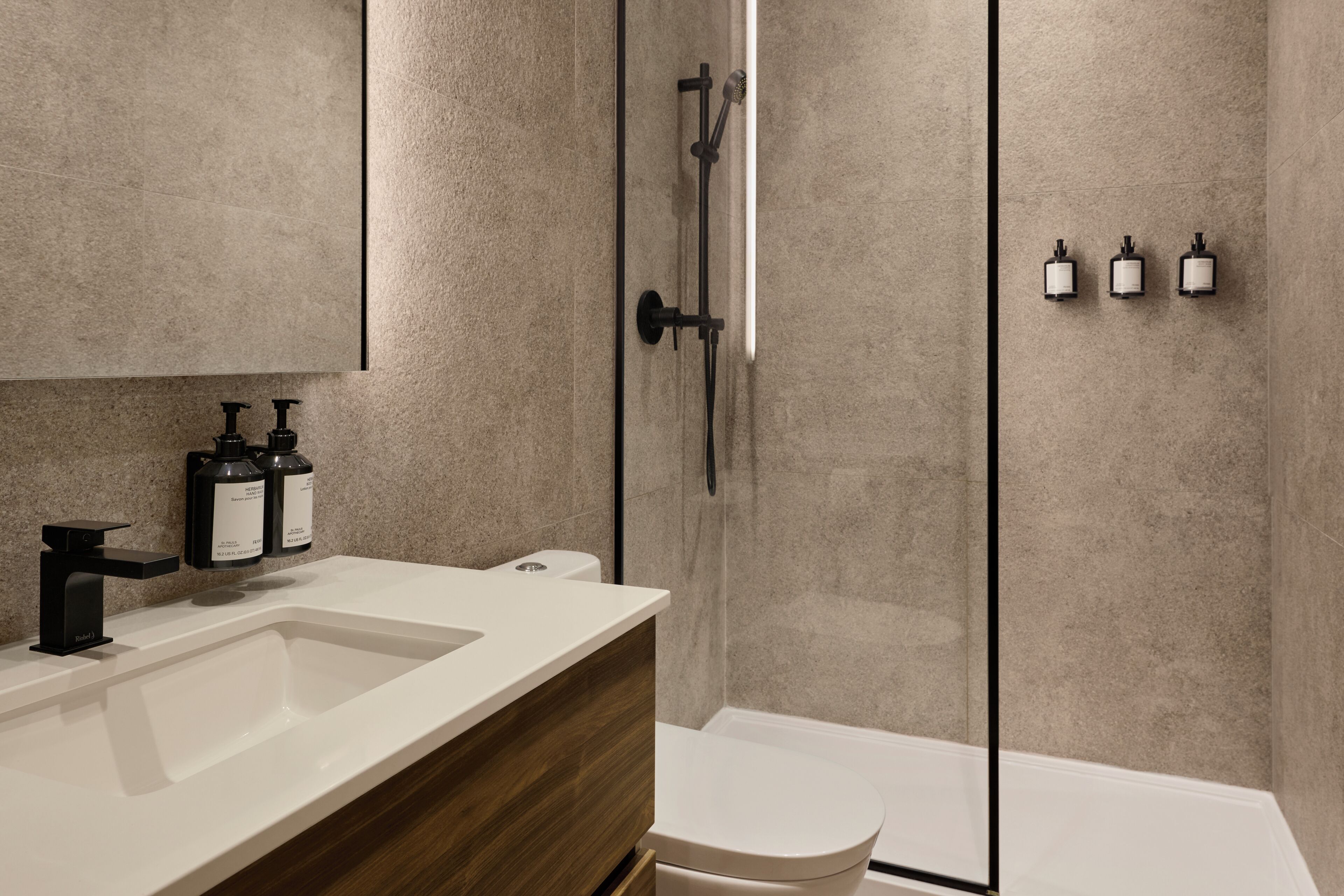 A modern bathroom with a glass shower enclosure, a white sink, and two soap dispensers.