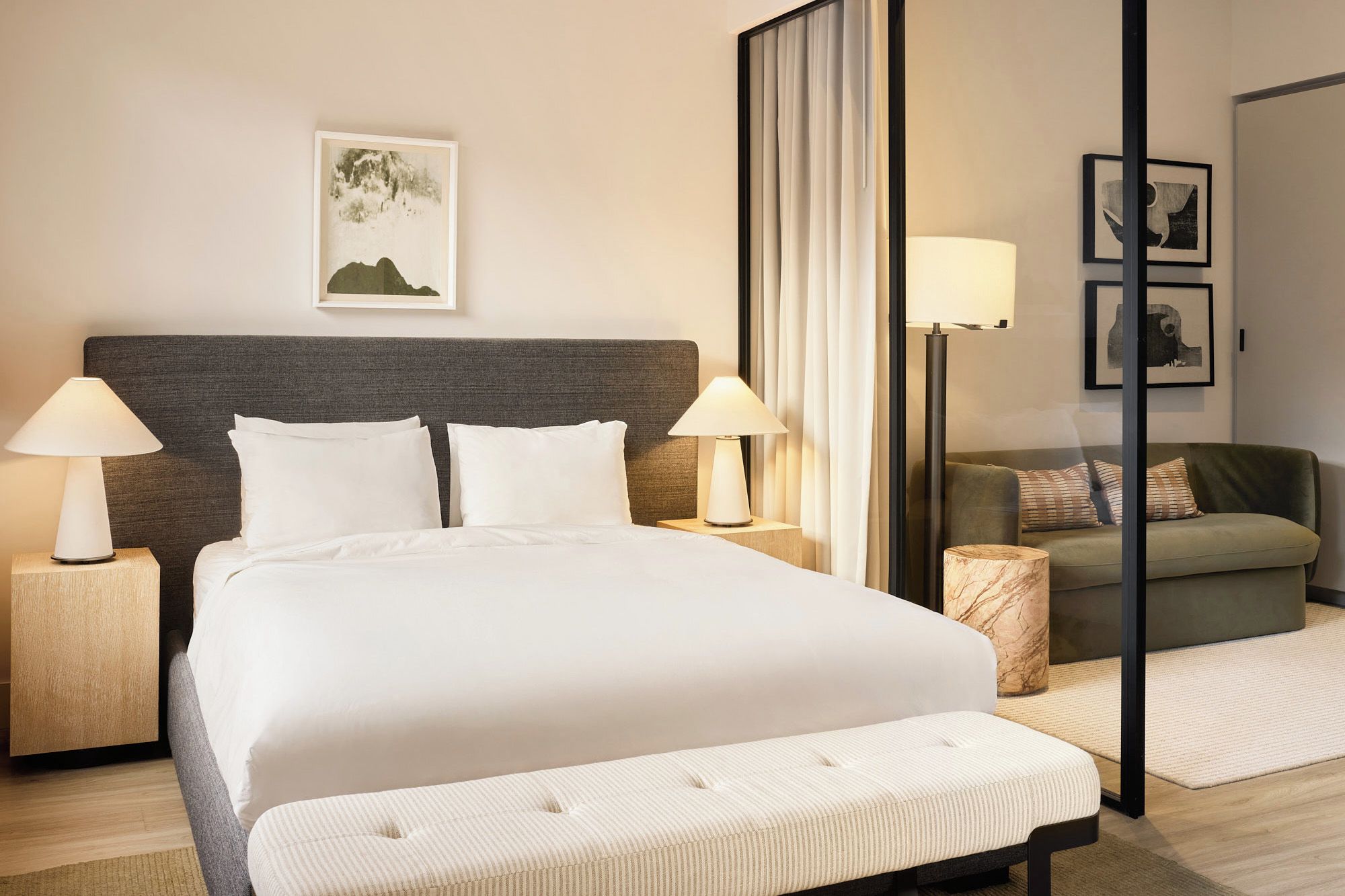 Una habitación de hotel con una cama grande, dos lámparas de noche, un sofá, una mesita y un cuadro en la pared.